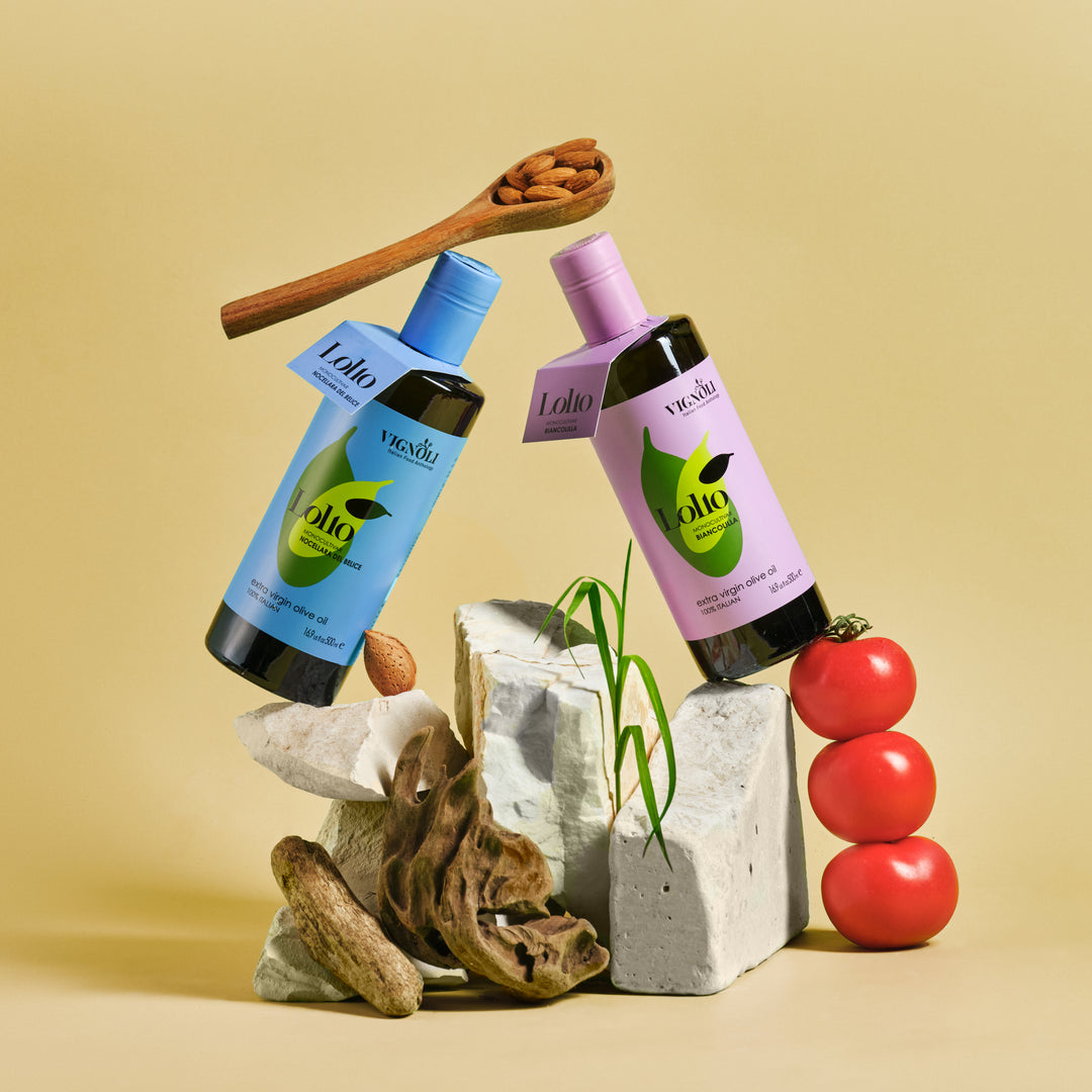 Biancolilla Monocultivar Extra Virgin Olive Oil front of 16.9fl oz bottle on rocks with tomatoes and nuts